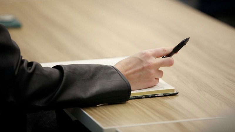 A person at a table taking notes in a notebook.