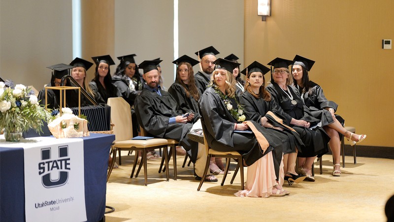 Students at USU Moab sit in cap and gown during commencement