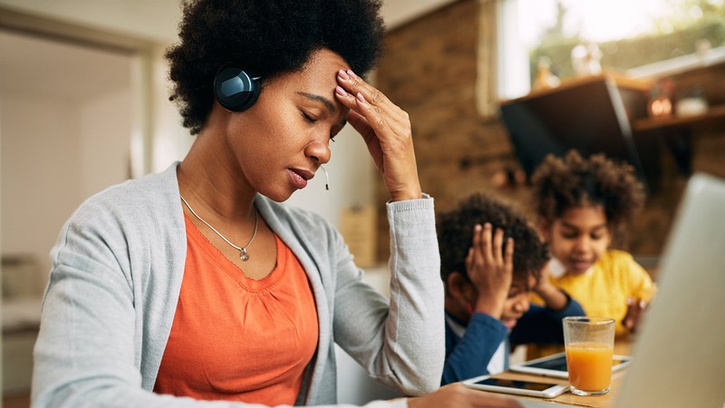 Woman working on a computer while children play in the background.