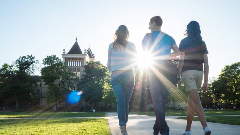 Three people walking on the Quad towards Old Main.