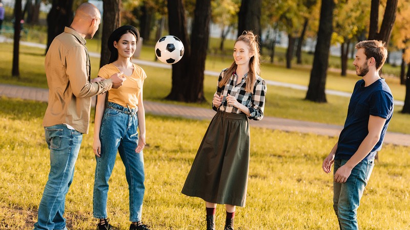 Young adults playing with a soccer ball at a park.