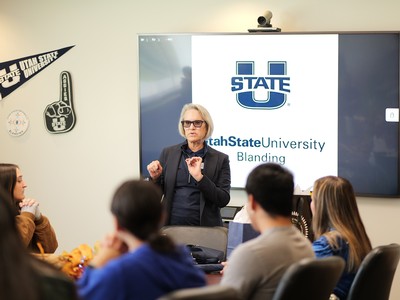A woman addresses a crowd in front of a room