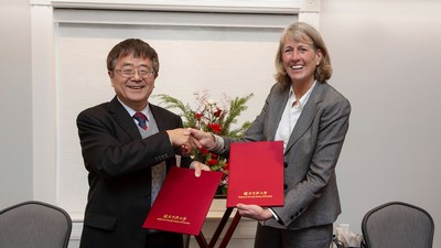 University presidents shaking hands while holding documents.