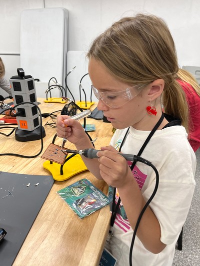 A girl solders a project in a lab classroom.