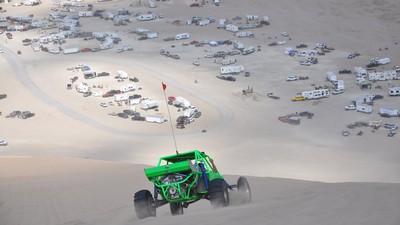A dune buggy driving down a slope overlooking a sprawling RV park.