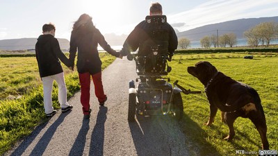 family with dog walking beside a family member with a motor-powered wheelchair