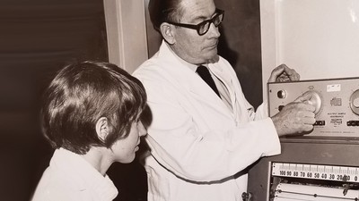 A black-and-white historical photo of R. Gaurth Hansen demonstrating a scientific instrument.