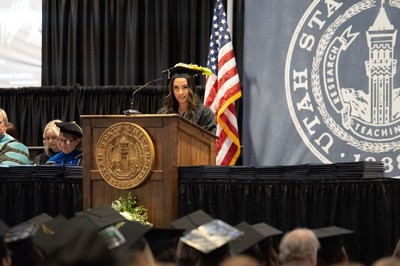 Thao Chau, wearing graduation regalia, speaks from a podium.