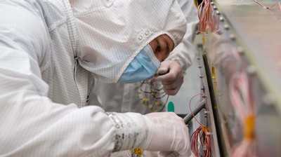 A person wearing protective equipment works on a scientific instrument.