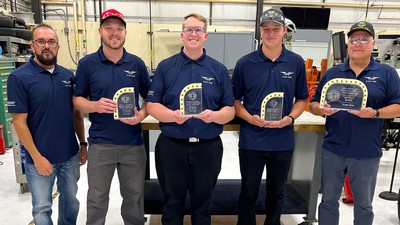 People holding trophies in a mechanic's shop.