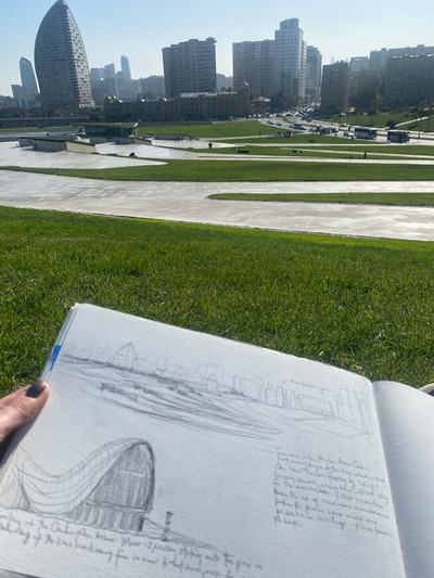 A person holding a sketchbook with a park in the background.