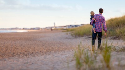 A father carrying a child on a beach.