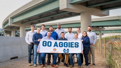 Engineers posing with a banner that says "Go Aggies" near a new highway interchange.