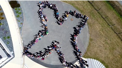 An aerial view of people standing in the outline of the letter X.