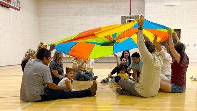 Parents and children play with a parachute in a school gym.