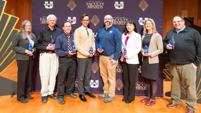 Faculty members hold awards at a ceremony.