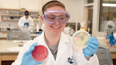 A scientist holding up Petri dishes with decorative designs growing in them.