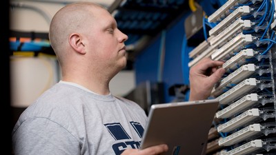 A worker inspecting computer networking hardware.