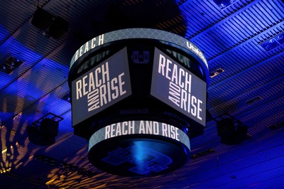 The video display in a basketball arena displaying the words "Reach and Rise."
