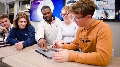 People looking at a tablet in a classroom with video conferencing screens.