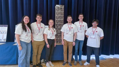 A group of students posing for a picture with a balsa model of a building.