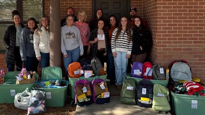 Volunteers stand behind several backpacks and supplies.