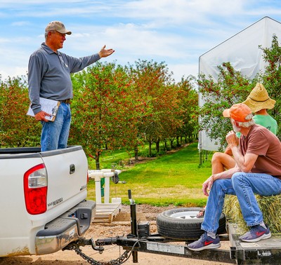 Brent Black standing in the bed of a pickup truck and talking to people at a fruit orchard.