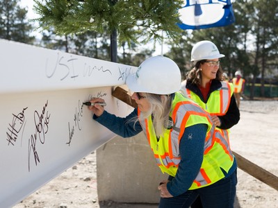 A woman signs her name to a steel beam while wearing construction gear.