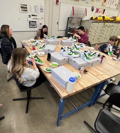 Students painting a green camo design onto sneakers.