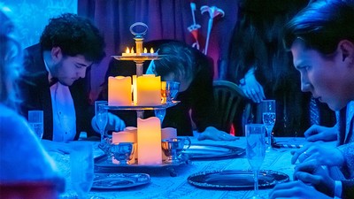 Actors in formal wear at a dinner table.