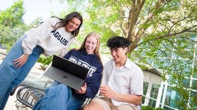 Students outside looking at a laptop.