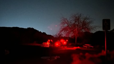 Skywatchers holding red flashlights in a campsite at night.