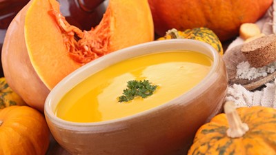 A bowl of pumpkin soup and some pumpkins.