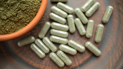 Ground herbs in a bowl and in pill capsules.
