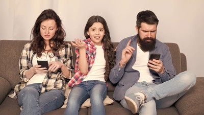 A child showing frustration as two adults ignore her to use their phones.
