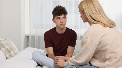 A mother speaking to a teenager in a bedroom.