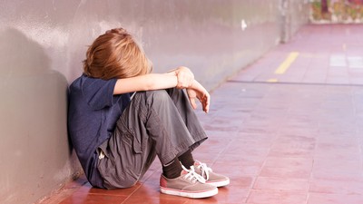 A child sitting on the ground alone with their head in their arms.