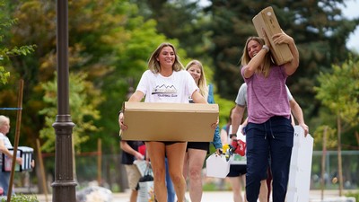 Two women carry boxes as they move things into a dorm room