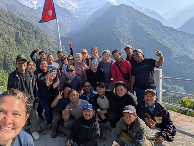 People posing for a photo with a Nepalese flag at a mountainous overlook.
