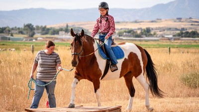 A person riding a horse while an instructor leads it.