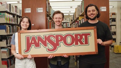 People in a library holding a hand-painted JanSport sign.