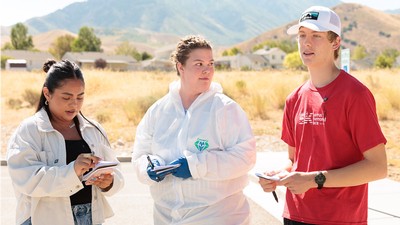 Students outdoors and taking notes while wearing personal protective equipment.
