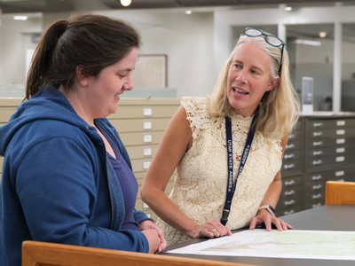 Two women discuss a map in a library.