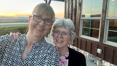 A mother and daughter take a photo outside a home at sunset, with a view of Cache Valley.