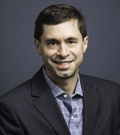 A man in a black suit and blue shirt poses for a headshot.