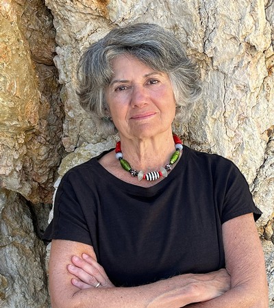A woman in a black shirt poses with folded arms against a jagged stone background.