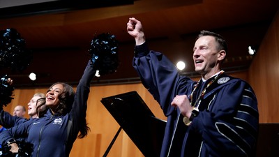 A man in regalia throws his hands in the air as part of the school fight song.