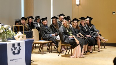 Students at USU Moab sit in cap and gown during commencement