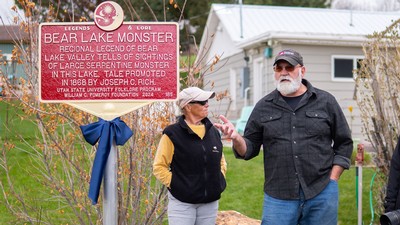 Teo people stand near a marker near a lake.