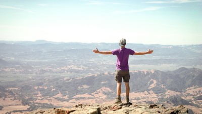 young man standing on a mountain and overlooking a valley.